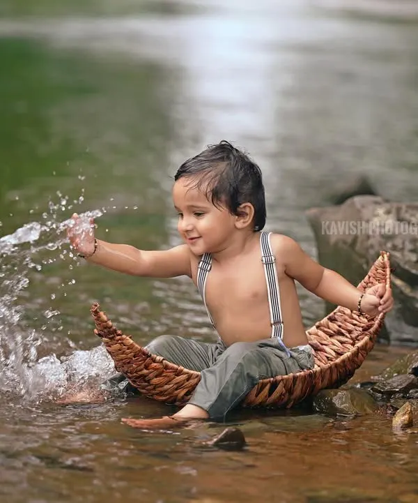 A joyful shot of a little boy splashing water while sitting in a small, rustic boat. Outdoor sessions like this allow for spontaneous and fun moments.