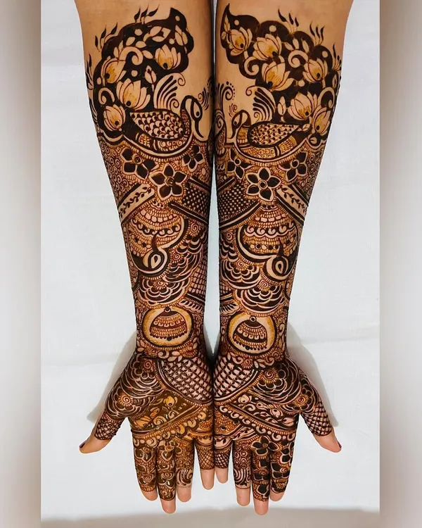 This engagement mehendi showcases a blend of traditional motifs. It features proud peacocks and blooming gulf flowers, creating a full and festive design that extends up the forearm.