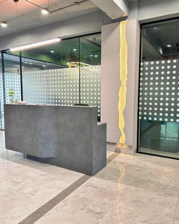 The reception area of a Gurugram corporate space, featuring a minimalist concrete-finish desk and a unique, river-like lighting feature. The design sets a clean, modern, and sophisticated tone for visitors.