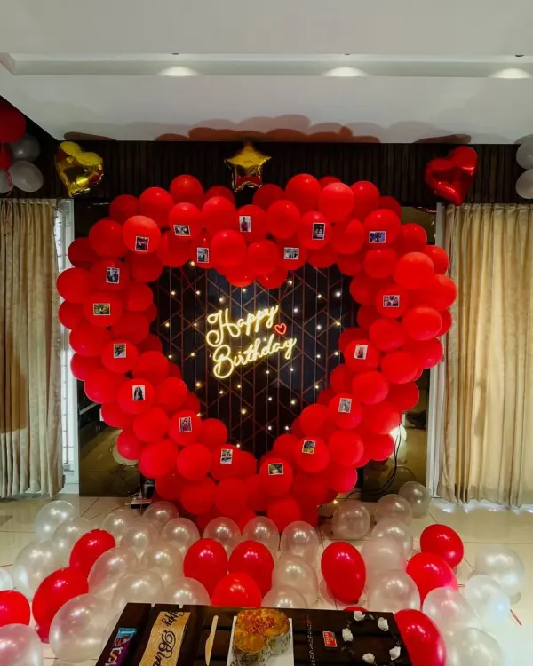A grand romantic gesture for a birthday. This large heart-shaped balloon frame is decorated with small photos of the couple and has a "Happy Birthday" neon sign in the center, creating a beautiful and personal backdrop.