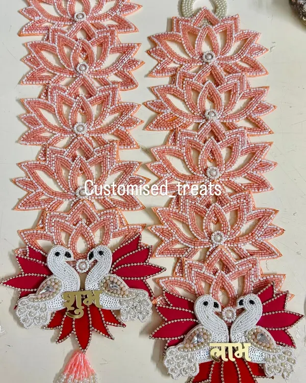 This elegant Shubh Labh set features swan motifs on a base of red leaves, with strings of beaded lotuses. It's a unique design for a modern yet traditional home.