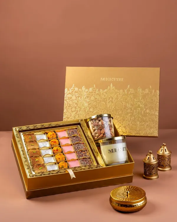 A festive gift box for Meethi India, featuring an assortment of Indian sweets, a scented candle, and dry fruits. The styling is elegant and targeted towards the luxury gifting market.