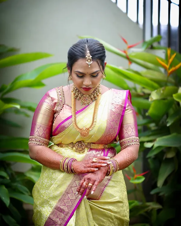 A bride in a moment of quiet reflection, wearing a traditional Kanjeevaram saree with a custom-designed pink and gold embroidered blouse.