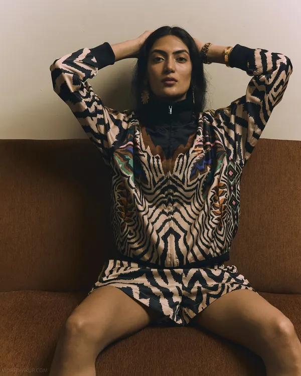 A bold, confident pose from a fashion editorial. The model's direct eye contact and powerful stance on the couch perfectly match the energy of the vibrant, animal-print outfit.