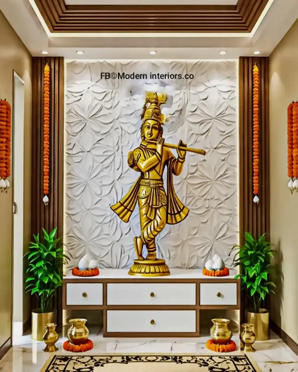 A beautiful pooja unit featuring a large brass Krishna idol against a 3D floral-patterned white backdrop. The unit includes drawers for storage and is framed by wooden slats and traditional marigold garlands.