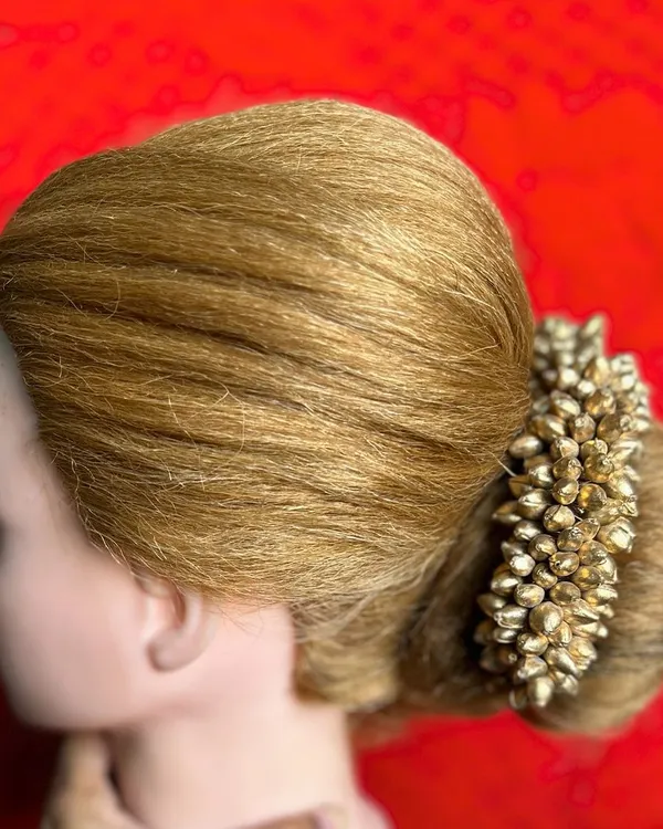 A side profile of a classic bridal bun adorned with a gajra of golden buds. In my course, you will learn how to create a smooth, perfectly rounded shape and secure heavy accessories.