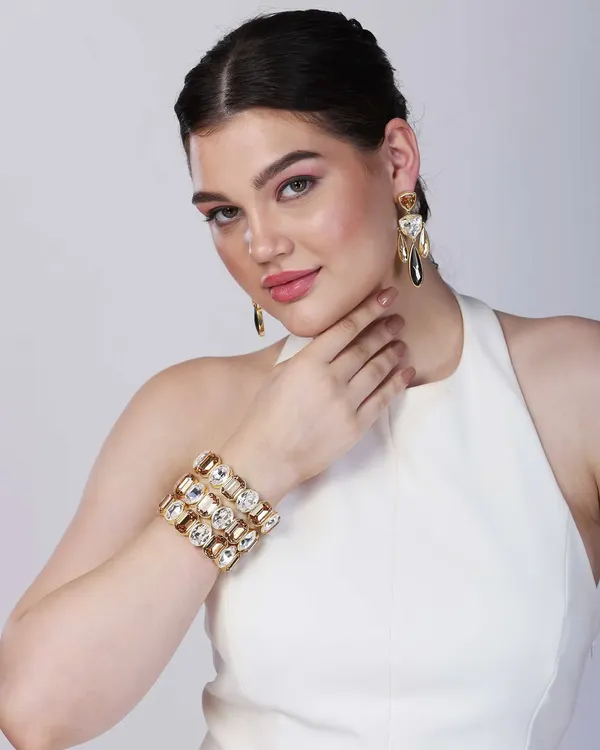 A striking close-up of a model wearing a bold, crystal-studded cuff bracelet and matching earrings. The direct gaze and clean lighting make this a powerful hero shot for a contemporary jewellery brand's homepage or ad campaign.