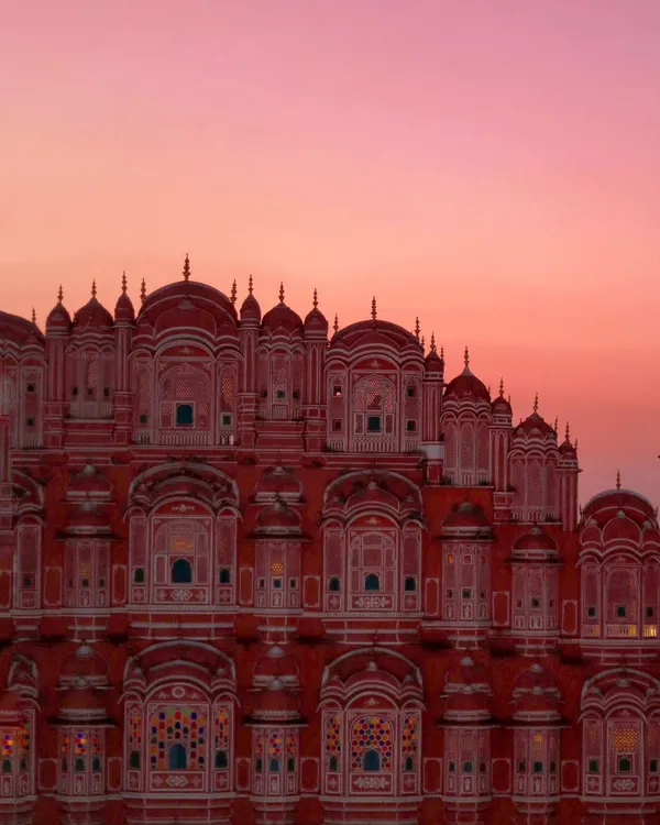 The iconic Hawa Mahal in Jaipur glows under a pink and orange sky. Capturing this landmark at sunset reveals why Jaipur is called the Pink City, a truly magical sight.