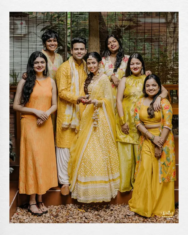 A happy group photo of the couple with their family and friends during their Haldi ceremony, all dressed in beautiful shades of yellow.