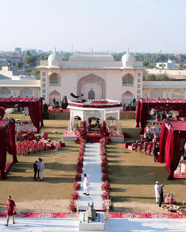 A breathtaking aerial view of the sundowner wedding setup at Anantara Jaipur. The grand scale of the palace architecture is balanced by the striking red and white decor, creating a truly royal path for the couple's ceremony.