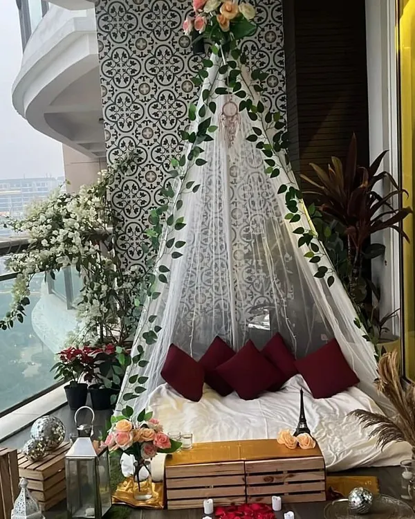 This is the daytime view of our romantic proposal teepee, set up on an apartment balcony. The sheer fabric, ivy vines, and floral accents create a beautiful and serene setting before it transforms with lights at night.