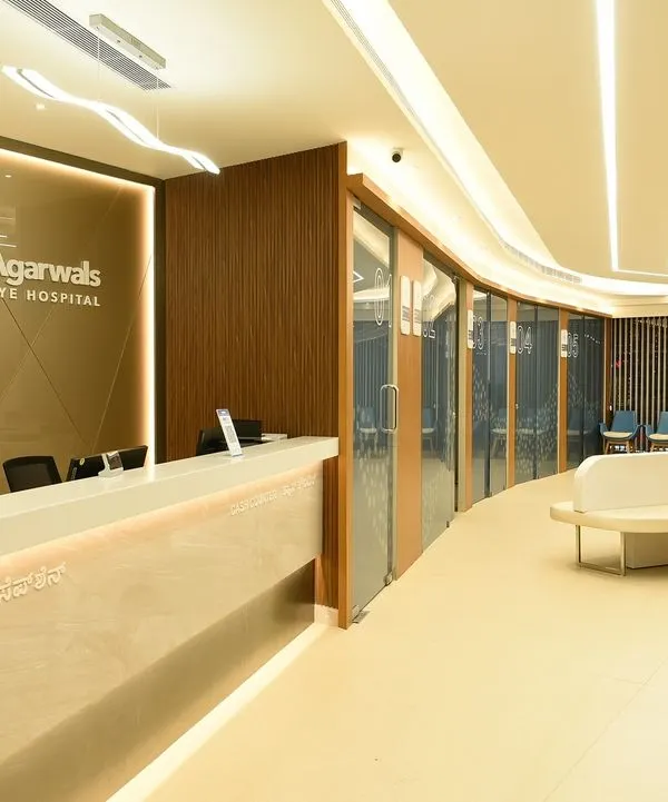 The main reception and waiting area at Dr. Agarwal’s Eye Hospital in Bangalore. The curved reception desk and flowing ceiling lights guide patient movement, while the wood and light color palette creates a welcoming atmosphere.