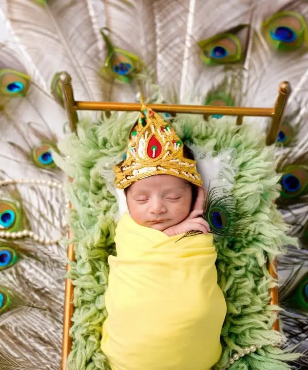 Our littlest Krishna, sleeping peacefully on a bed of peacock feathers. This stunning overhead shot is a unique and artistic way to capture your newborn during the festive season of Janmashtami.