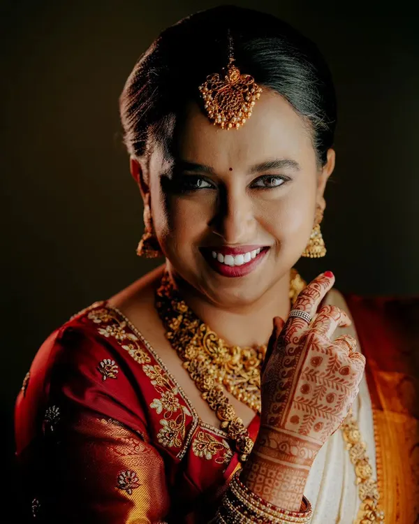 A classic, close-up bridal portrait. This shot focuses on the bride's radiant smile, detailed henna, and traditional gold jewelry.