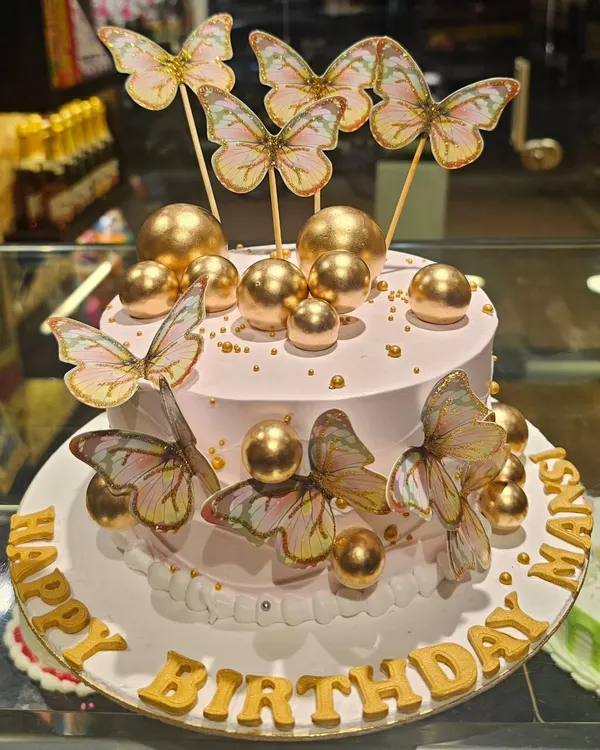 An ethereal and glamorous birthday cake. This design features a soft pink frosting, a cascade of golden spheres, and delicate wafer paper butterflies, creating a dreamy and elegant look.