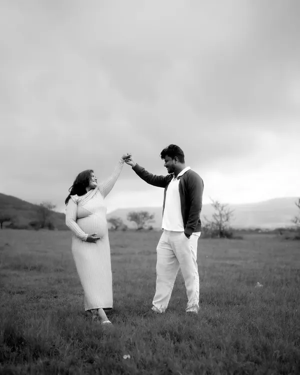 A timeless black and white photograph of a couple sharing a dance in an open field. This image captures the romance and joy of their journey together as they await their new arrival.