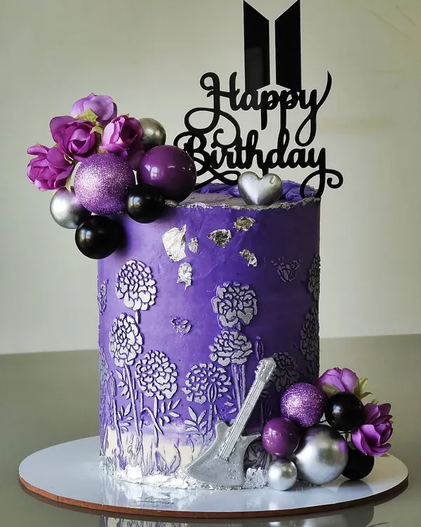 A cake for the BTS army. This design is in the signature purple, with a silver floral bas-relief texture, a guitar accent, and the iconic BTS logo topper, making it a perfect tribute to the band.