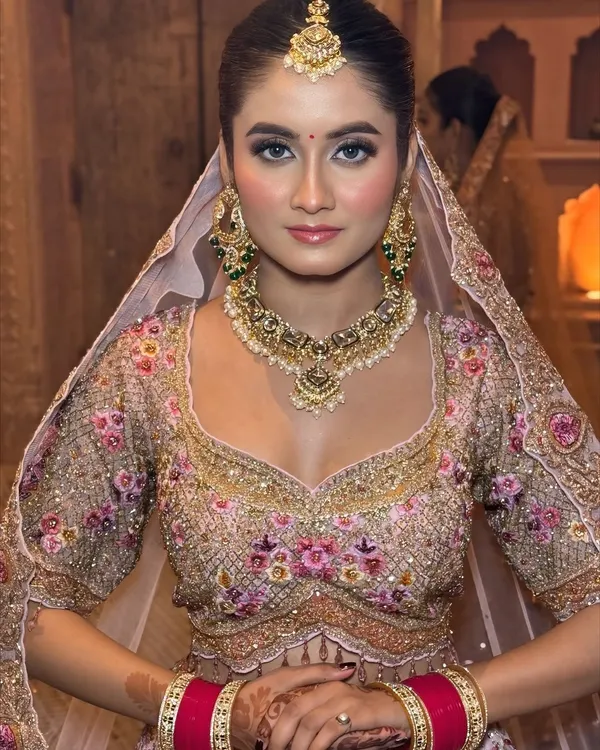 A stunning portrait of a bride in a pastel floral lehenga. The makeup is soft and dewy, with a focus on clean skin and defined eyes for a modern, ethereal look.