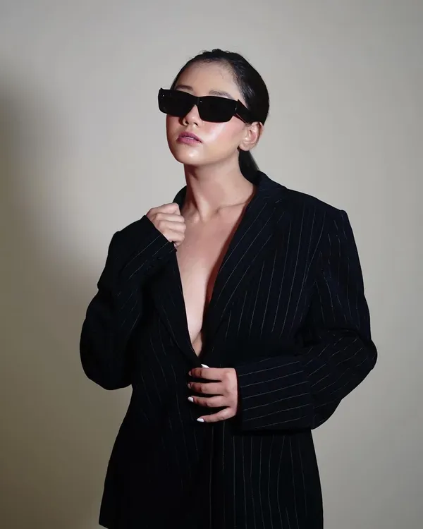 A confident pose that embodies the 'boss lady' vibe of this shoot. The simple background and focused lighting put all the attention on the model's attitude and the sharp lines of the blazer and sunglasses.