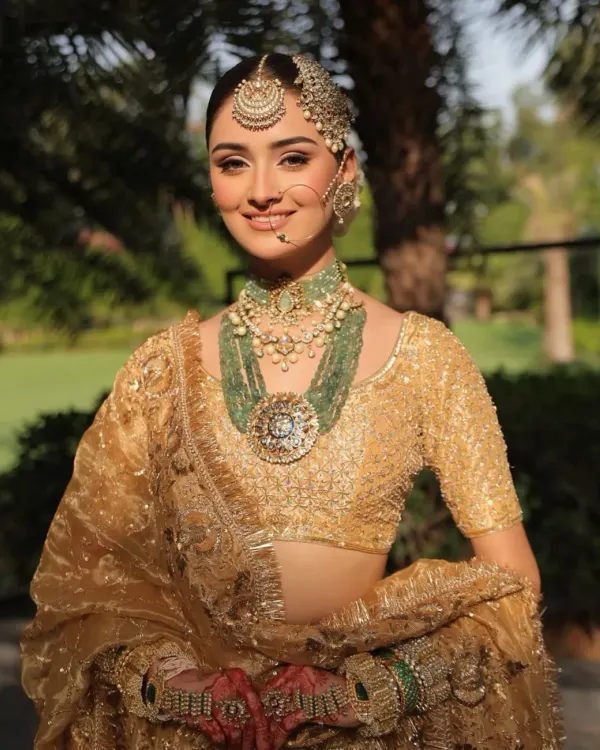 A classic bridal portrait in a shimmering gold lehenga. The look is elevated with layered emerald and polki jewelry, creating a regal contrast that is both traditional and breathtakingly beautiful.