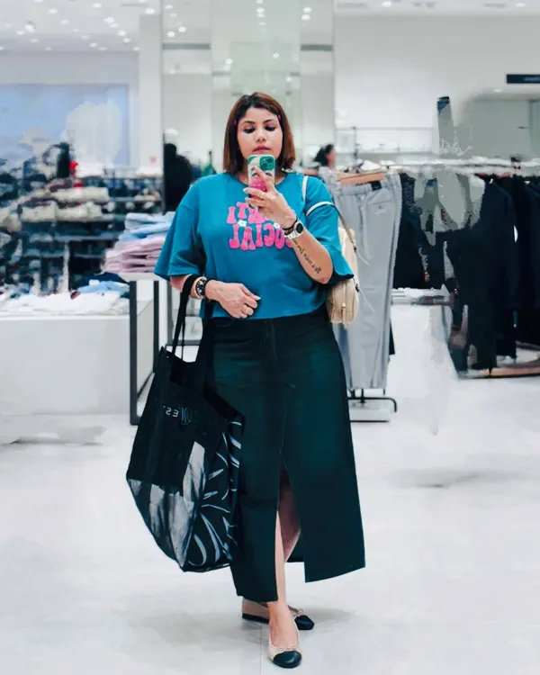 A casual shopping day look captured in a store mirror. A graphic blue tee paired with a dark denim skirt is a comfortable and cool combination for a day on your feet.