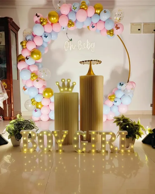 A classic gender reveal setup with a gold ring arch. The arch is decorated with pink and blue balloons, gold accents, and butterfly details, with a neon "Oh Baby" sign and "BOY or GIRL" marquee letters.