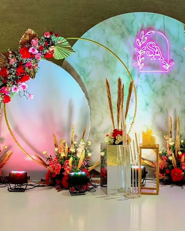 This modern photo-op stage features two large circular backdrops with a marble-effect finish, accented with bold red floral arrangements and a custom neon sign.
