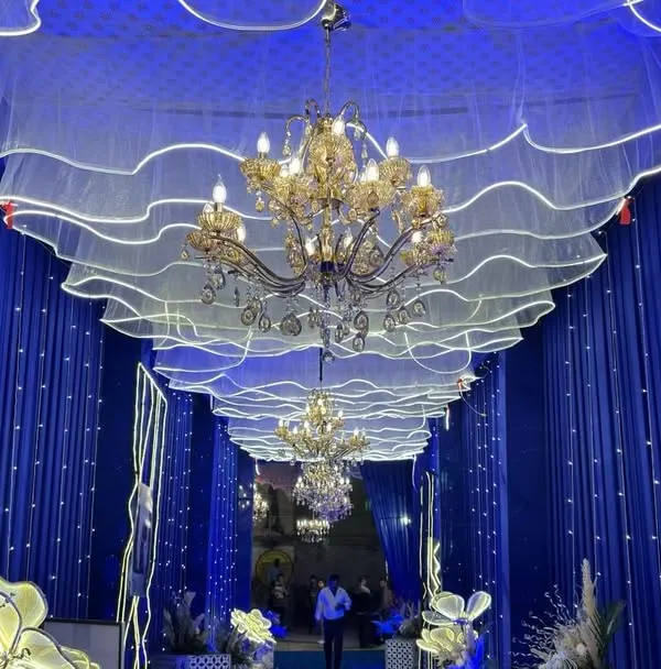 An immersive entrance passage created with royal blue draping, elegant chandeliers, and custom wavy ceiling panels with integrated lighting. We design grand entrances that wow your guests from the first step.