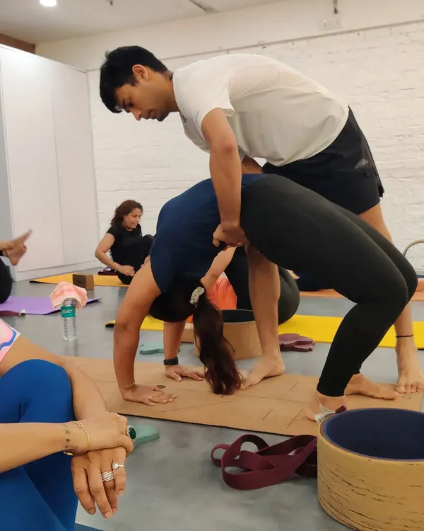 An instructor provides a hands on adjustment in Urdhva Dhanurasana, or Wheel Pose. This careful guidance helps the student lift and open their chest safely, ensuring the backbend is distributed evenly along the spine to prevent strain.