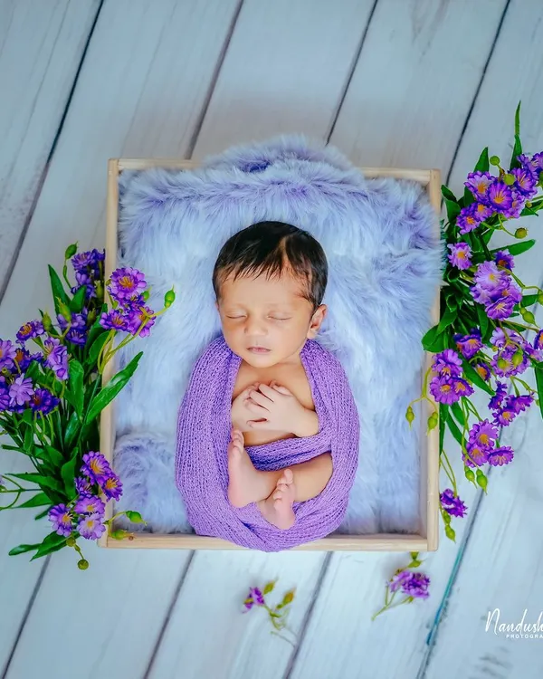 A beautiful example of a color-themed newborn shoot. Here, a soft purple wrap and matching flowers create a rich, vibrant portrait, highlighting the baby's peaceful expression while nestled in a fur-lined box.