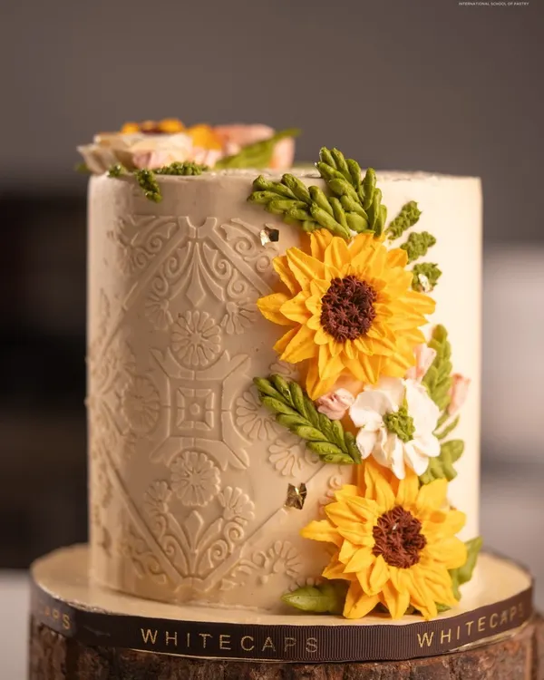 An elegant custom cake featuring intricate patterns and delicate, handcrafted buttercream sunflowers. I create these bespoke designs to make your celebrations truly beautiful and unique.
