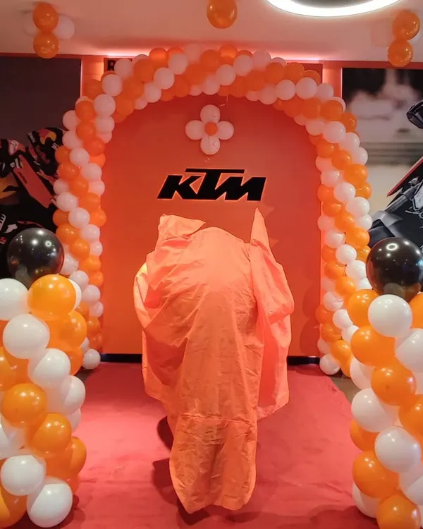 This setup for a KTM motorcycle launch features a balloon arch and pillars designed with the company's signature orange, white, and black brand colors. The decor builds excitement and draws attention to the new product reveal in the showroom.