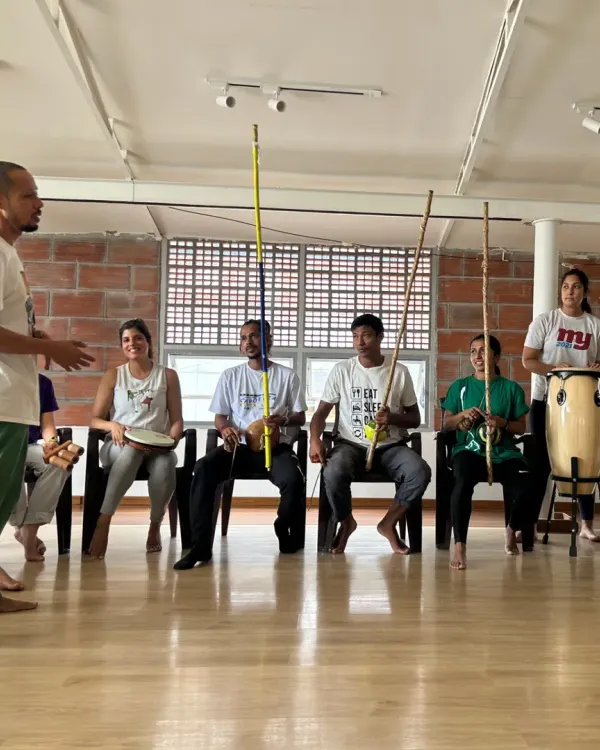 An instructor teaches the rhythm of the berimbau, the single-stringed instrument that leads the Roda. Participants learn to play instruments and contribute to the music.