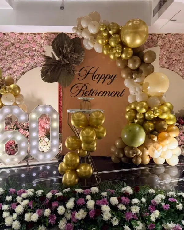 This was the main stage for a 60th birthday and retirement party. The setup featured a beautiful pink floral wall, a custom backdrop, marquee numbers, and a gold and white balloon arch, creating an elegant and celebratory focal point.