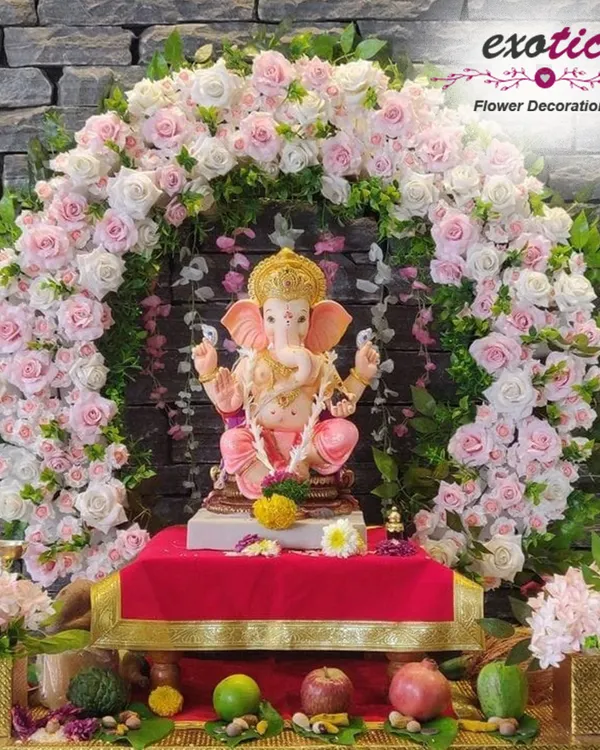 A beautiful and classic Ganpati decoration. This perfectly shaped arch of pink and white roses provides a delicate and respectful frame for the Ganesha idol, set against a stone wall.