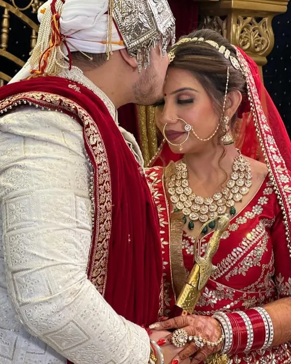 A beautiful, candid moment between the bride and groom. Her classic red lehenga and soft glam makeup create a timeless picture of wedding day happiness.