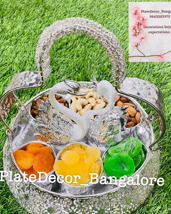An ornate silver basket with swan figurines, filled with different compartments of dry fruits like cashews, almonds, and candied fruits.