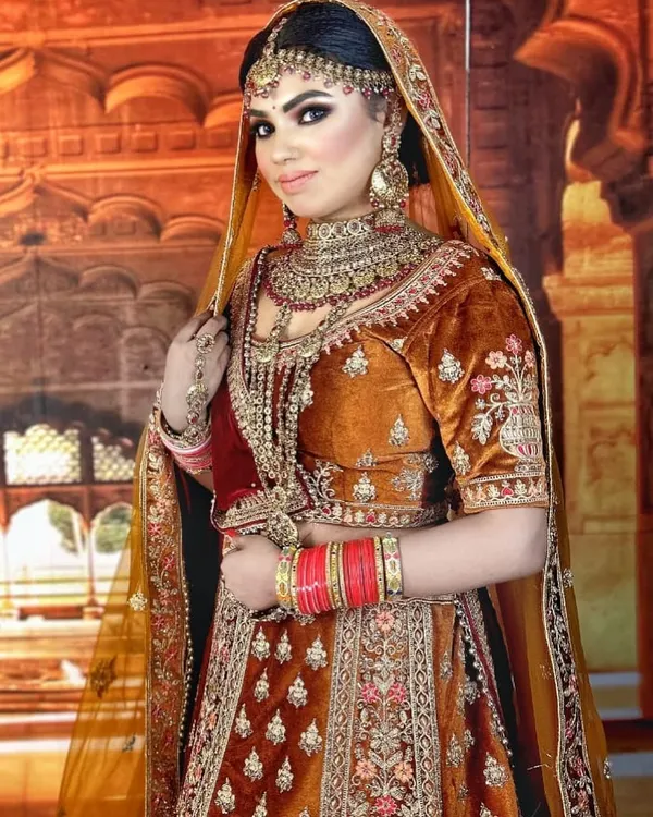 A classic bridal look in a rich rust-orange velvet. This rental lehenga features traditional embroidery and is paired with heavy kundan jewellery, perfect for a timeless wedding ceremony.