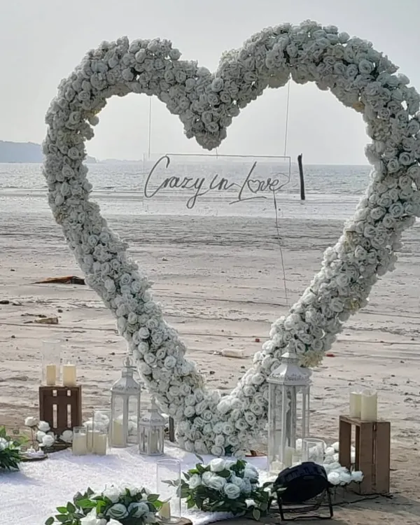 A close-up of our 'Crazy in Love' beach proposal decor. The large floral heart arch, surrounded by lanterns and candles, creates a stunning frame for the big question.