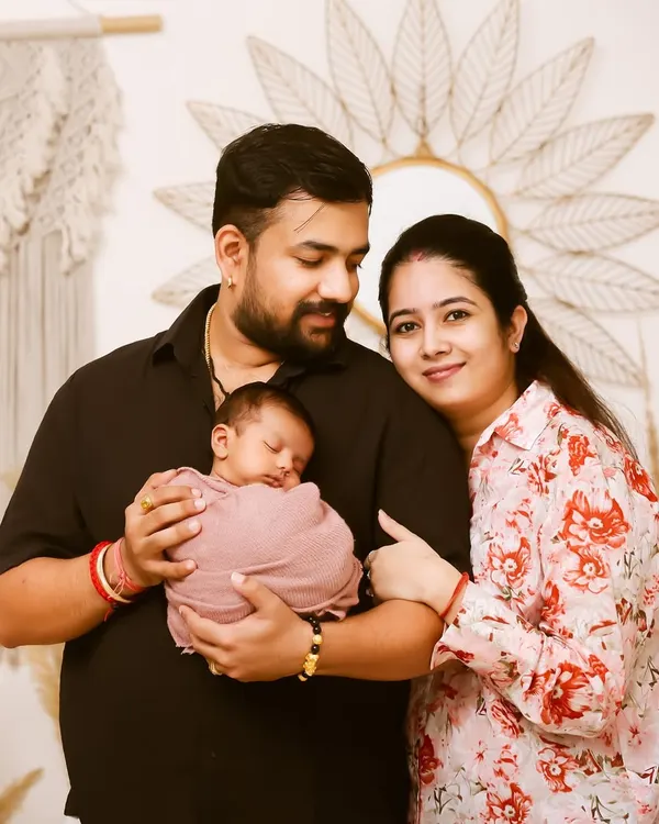 A beautiful first family portrait. The new parents gaze lovingly at their sleeping newborn, wrapped snugly in pink, in a warm and natural studio setting.