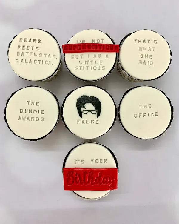 An overhead shot of "The Office" themed cupcakes, showcasing the detailed fondant work with quotes like "That's what she said" and "Bears. Beets. Battlestar Galactica."