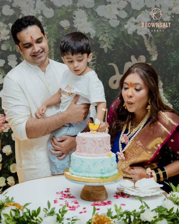 A beautiful family celebrating a baby shower. The mother-to-be is blowing out the candle on a two-tiered pink and blue cake, a sweet moment of anticipation.