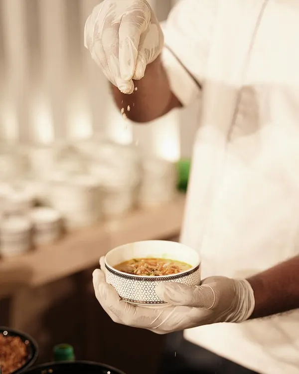 A chef adds the final garnish to a bowl of Burmese Khow Suey. This coconut-infused noodle soup is a customizable delicacy, allowing guests to add their own fresh and fried toppings for a personal touch.