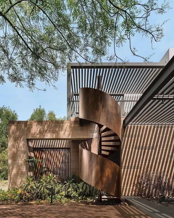 We believe great architecture is a form of poetry. This Ahmedabad home by Khosla Associates masterfully plays with light and shadow, using a sculptural corten steel staircase and slatted pergolas to create a dynamic experience that responds to the sun's movement.