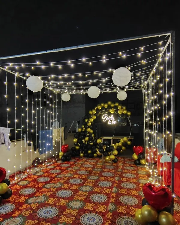 A full view of a 'Bride to be' terrace party setup. I used a canopy of fairy lights and paper lanterns to create a magical ambiance around the black and gold balloon photo booth.
