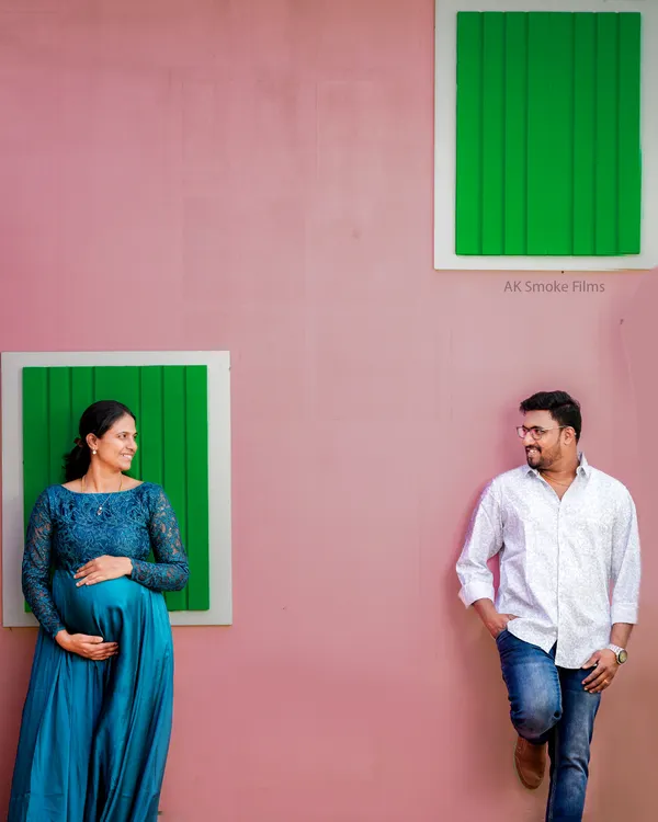 A modern and stylish couple's portrait using bold colors and composition. The pink wall and green windows create a vibrant, playful backdrop for this contemporary maternity shoot.