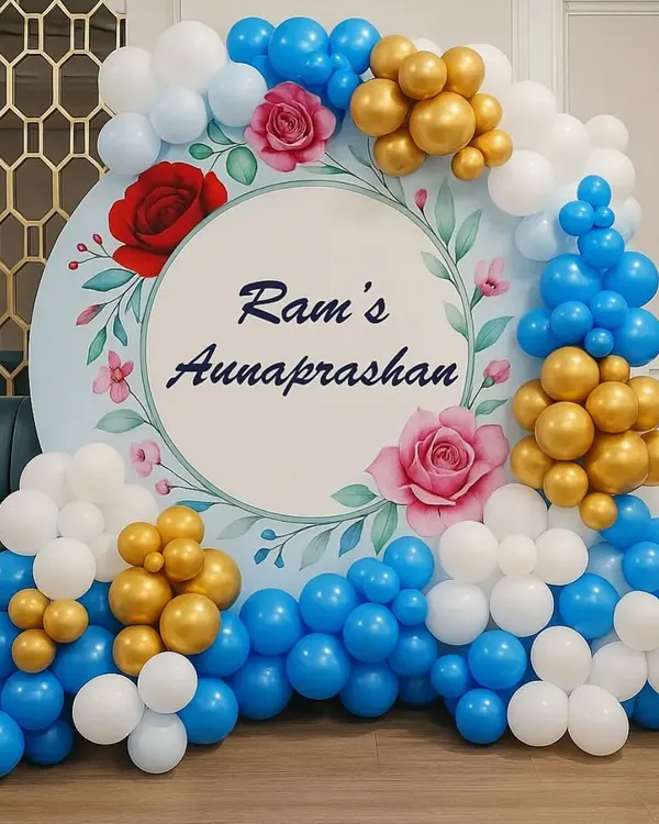 A beautiful backdrop for Ram's Annaprasan (first rice-eating ceremony). The circular backdrop has a floral design and is framed by a blue, white, and gold balloon arrangement.