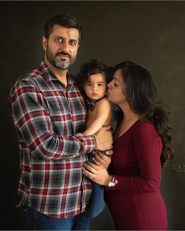 A warm and intimate family portrait. The dark background helps to emphasize the connection and love between the parents and their child.