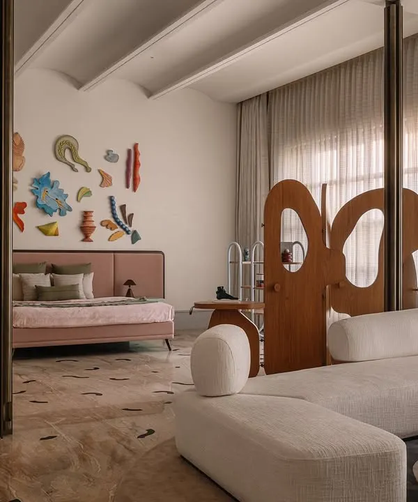 This junior master bedroom at Rehethaan is designed to feel like a private gallery. A sculptural wooden screen divides the sleeping and lounging areas, while a colorful art installation and custom furniture create a playful, sophisticated vibe.