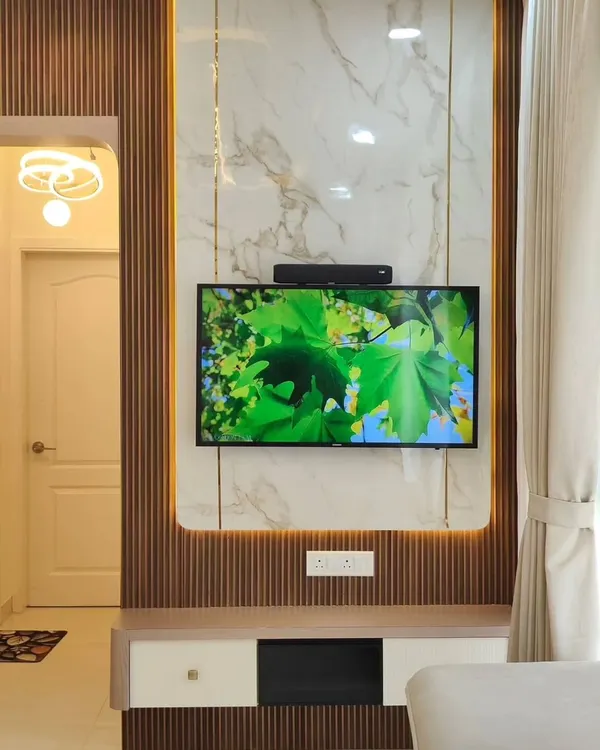 This full-height TV unit combines a white marble-finish backdrop with dark fluted wood panels. The warm LED backlighting creates a beautiful ambient glow, making the entertainment wall a stunning feature in the living room.